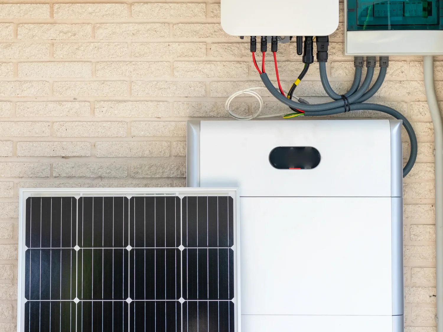 A wall mounted home battery, inverter and consumer unit beside a solar panel